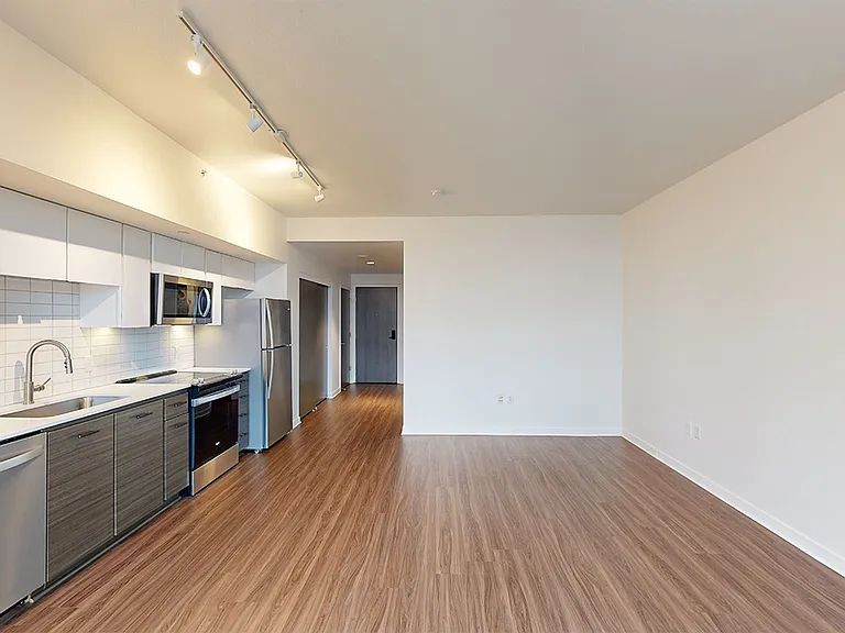 Apartment kitchen with stainless steel appliances, dining and living room with wood-style flooring.