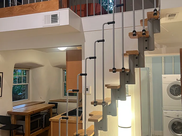 Open main level with newly furnished living area, kitchenette, counter-height dining space and sculptural staircase leading to the loft.