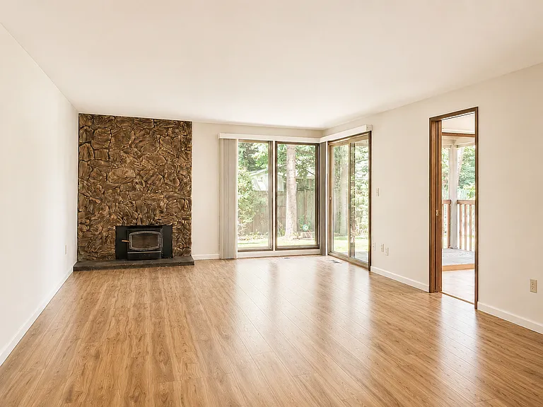 Dining Room/Living Room combination where the Living Room boasts a cozy wood-burning fireplace and a beautiful view of backyard through both floor windows and second sliding door to the deck