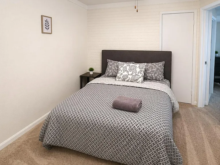 Private bedroom with plush carpet, ceiling fan, and textured accent wall, plus space for a nightstand and storage.
