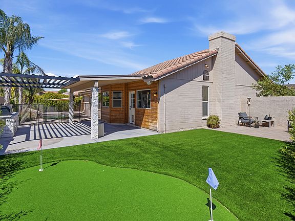 Backyard view with putting green, covered seating area, pergola, outdoor kitchen