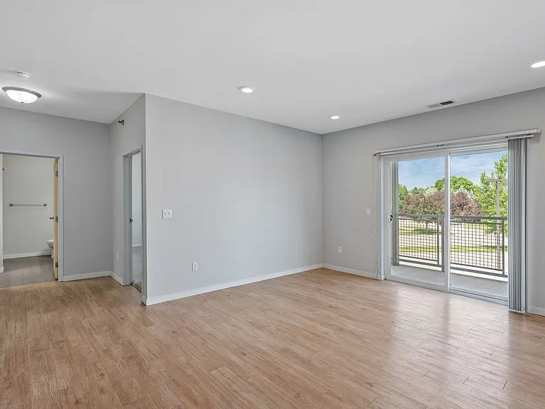 Bright and airy living space with large sliding glass doors leading to a balcony, featuring modern hardwood floors and soft gray walls. Bright and airy living space with large sliding glass doors leading to a balcony, featuring modern hardwood floors and