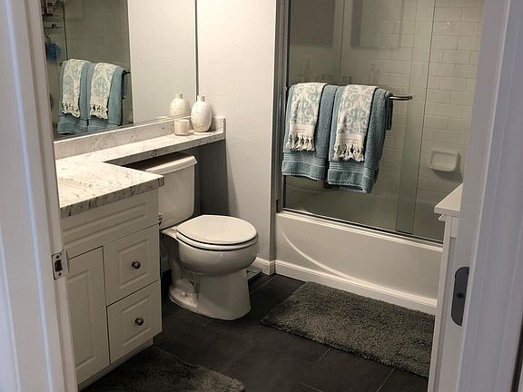 Calacatta marble counter top with updated tile flooring, subway tiles in shower with sliding glass doors.