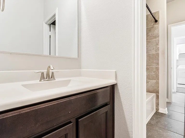 Bathroom vanity with a white countertop and integrated sink, brushed nickel faucet hardware, and dark wood-finish cabinetry