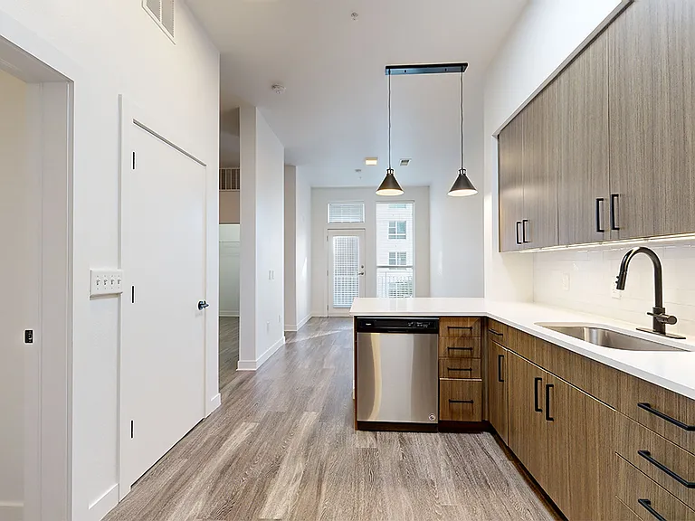 Apartment kitchen with stainless steel appliances, dining and living room with wood-style flooring.