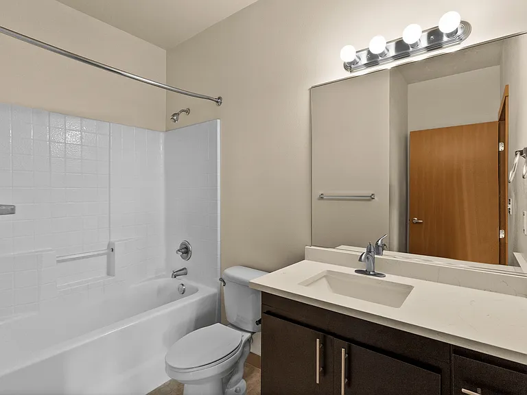 Modern bathroom featuring a sleek vanity with under-sink storage, bright lighting, and a clean bathtub with a curved shower rod. Modern bathroom featuring a sleek vanity with under-sink storage, bright lighting, and a clean bathtub with a curved shower ro