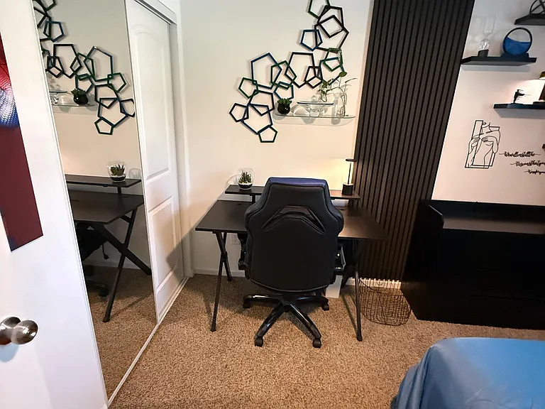 Carpeted bedroom with mirrored closet doors and a dedicated desk setup, offering a practical work-from-home corner.