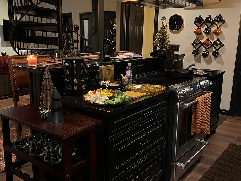 Electric stove/oven and stainless-steel vent-a-hood surrounded by granite countertops and wine storage cabinet.