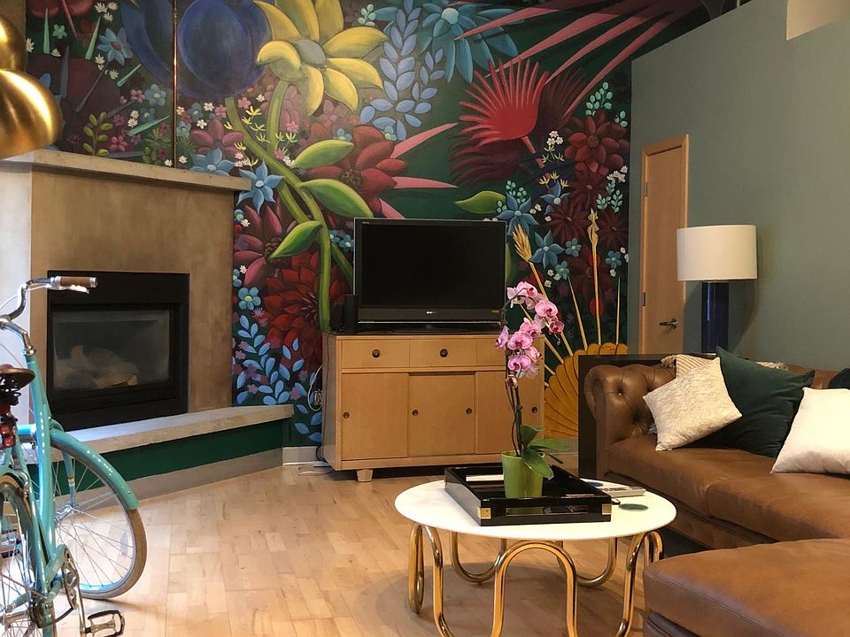 Main living space with mural by a local artist, fireplace, 13 ft ceilings, exposed brick, and huge windows with motorized blinds.