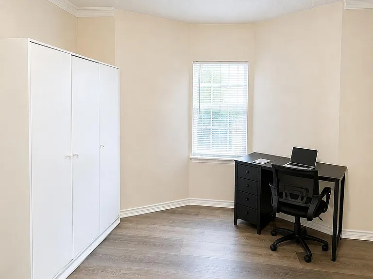 Spacious room with a large wardrobe, dedicated desk area, and a window for natural light over durable wood-look flooring.
