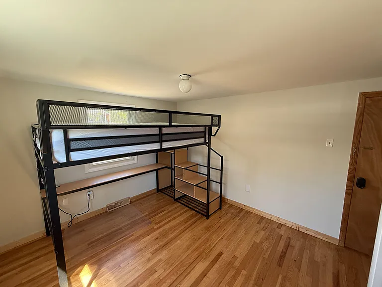Bedroom with hardwood floors, a loft-style bed frame with built-in shelving, and a window for natural light.