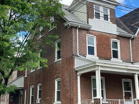 Corner brick building, front porch has room for chairs and table.