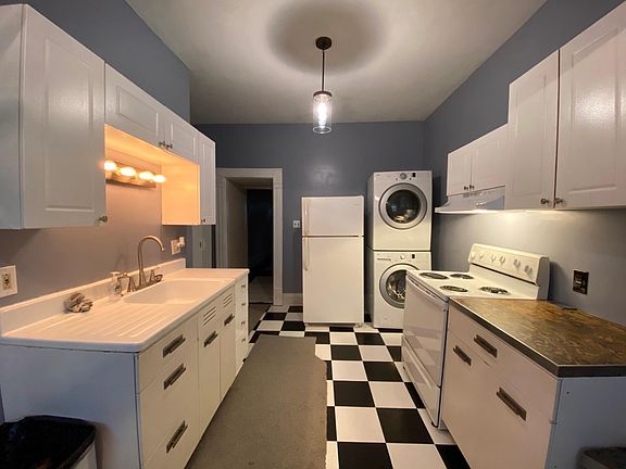 Kitchen - Restored antique farmhouse sink and prep table, full-size electric stove with range hood and fan, refrigerator, stack laundry units, dish cabinets, and standalone pantry cabinet. The gray rugs are just down to protect the floors while the place