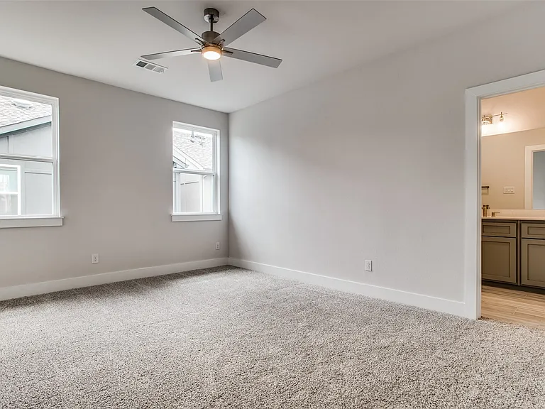 The large primary suite with ceiling fan and blinds on the windows.