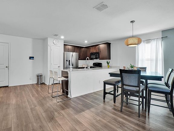 Open-concept kitchen and dining area featuring wood-finish flooring, dark wood cabinetry, stainless steel appliances, and a breakfast bar