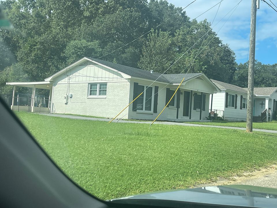 House view showing front, side and back of house where covered back patio is. Yard is fenced in. There are two large Satsuma trees and one fig tree in back yard.