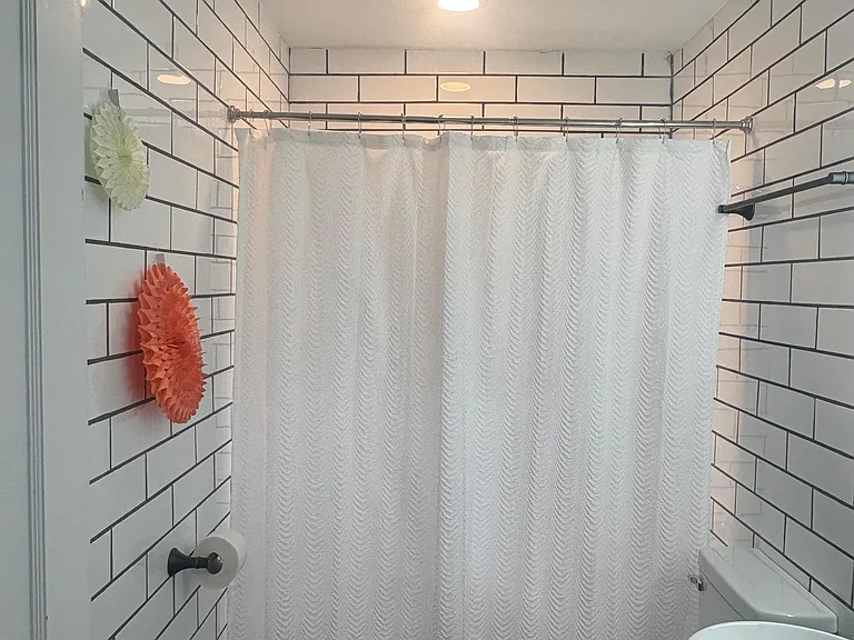 Bathroom with tiled tub/shower surround, curved shower rod, recessed lighting, and a vanity with vessel sink.
