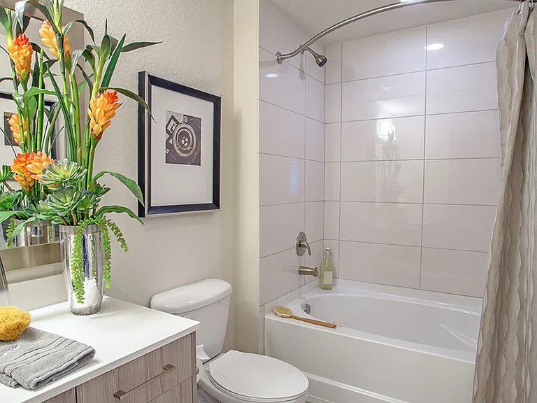 Luxury apartment bathroom with quartz vanity, soaking tub with tile surround, and modern fixtures
