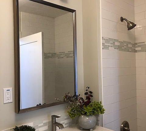 Beautiful bathroom with gray shaker vanity, tile floors, white quartz countertop, tub/shower combination with white subway tile surround with glass/marble accents.