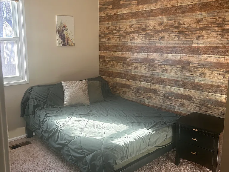 Third bedroom pictures a full size bed, desk/dresser combo, and lounge chair. Includes a feature wall for log cabin vibes and wood shelves.