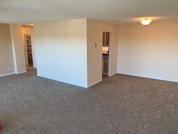 Living room view with dining area to the right. Kitchen is behind the wall. Hallway to bedrooms and bathrooms to the left.