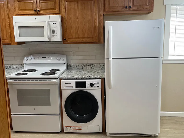 Kitchen has electric stove/oven with overhead microwave and combo washer/dryer and refrigerator/freezer