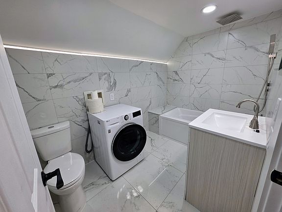 European tiled bathroom with 3 position shower, LED accent lighting, dual flush toilet, and high efficiency washing machine