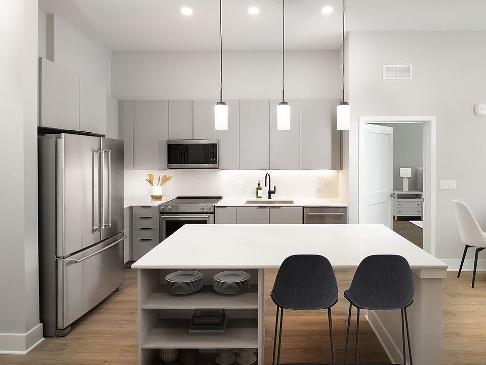 Signature Collection kitchen with stainless steel appliances, light grey cabinetry, marbled quartz countertops and backsplash, under-cabinet lighting, built-in shelves, and hard-surface flooring