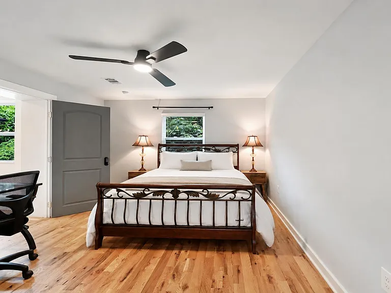 Spacious furnished bedroom with hardwood floors, ceiling fan, and a dedicated desk area.