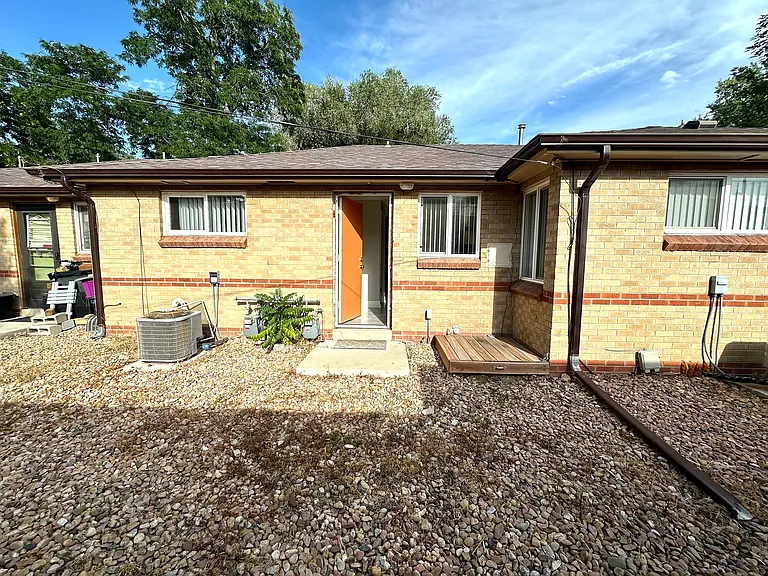 Charming brick exterior of a cozy home with a welcoming open door, surrounded by a low-maintenance rock garden and lush greenery.