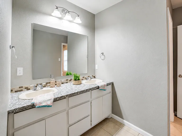 Shared Jack & Jill bathroom connecting Suites 1 & 2. Features a double-sink vanity with ample counter and cabinet space, bright lighting, and a full bathtub with shower. Each bedroom has its own private entrance for added convenience.