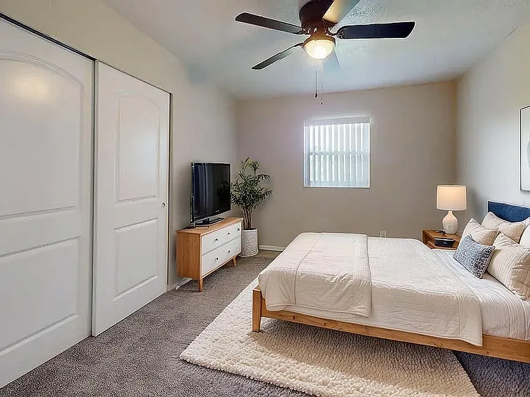 Bright and inviting bedroom with cozy carpet, modern ceiling fan, elegant decor, and ample storage space.