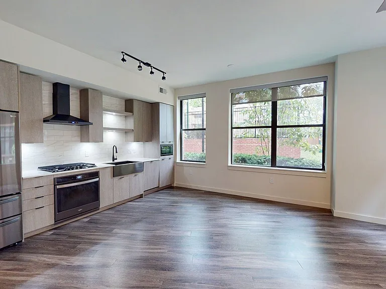Apartment kitchen with black stainless steel appliances, dining and living room with wood-style flooring.