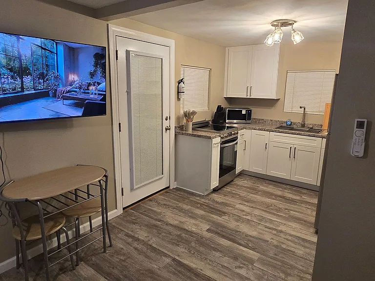 Compact eat-in kitchen with L-shaped counters, full-size range and sink, plus a small dining table and patio-door access.
