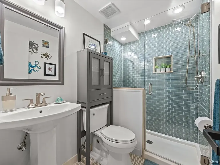 Bathroom with tiled floor, walk-in shower, storage unit, toilet and pedestal sink