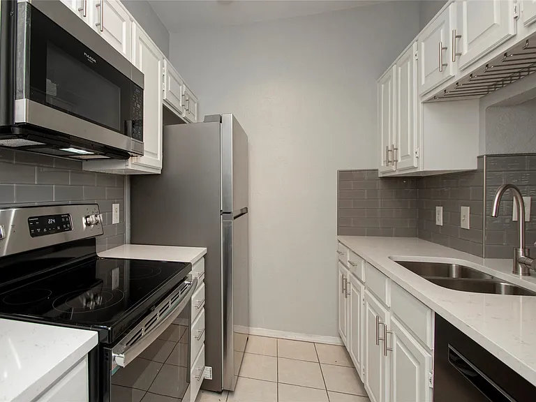 Updated kitchen featuring white shaker cabinetry, stainless steel appliances, light-toned countertops, and a gray subway tile backsplash