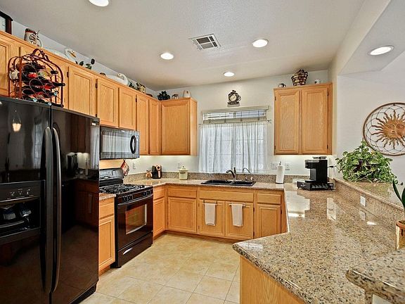 Beautiful kitchen boasting sleek black appliances, granite countertops, recessed lighting, and warm honey-hued cabinetry with breakfast counter that opens to the living area