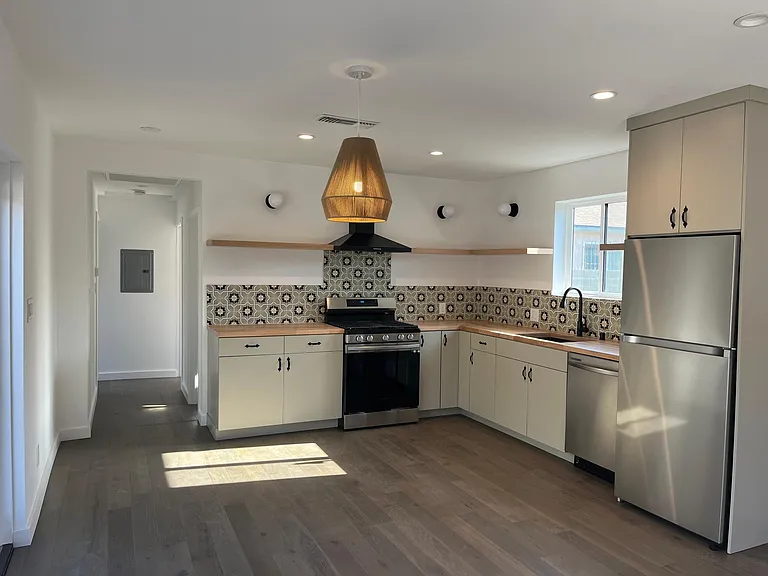 Open kitchen with full amenties, butcher block counter tops, windows casting light, recessed lighting, open shelving, dishwasher and luxe fridge.