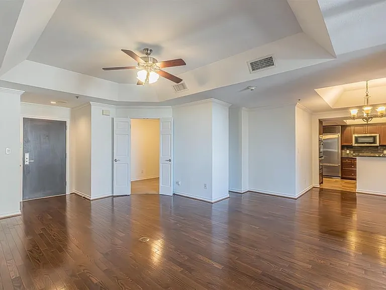 Spacious open-concept living area featuring rich wood-finish flooring, a tray ceiling with a ceiling fan, and white baseboards