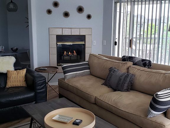 The living room and dining nook feature big windows with coverings, a door to a spacious balcony, a gas fireplace, and furnishings.