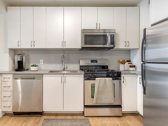 Renovated II North/South kitchen with stainless steel appliances, grey quartz countertops, white lacquer cabinetry, white tile backsplash, and hard surface flooring