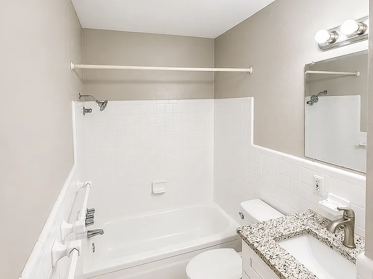 Modern bathroom featuring a sleek bathtub, elegant granite countertop, and bright vanity lighting.