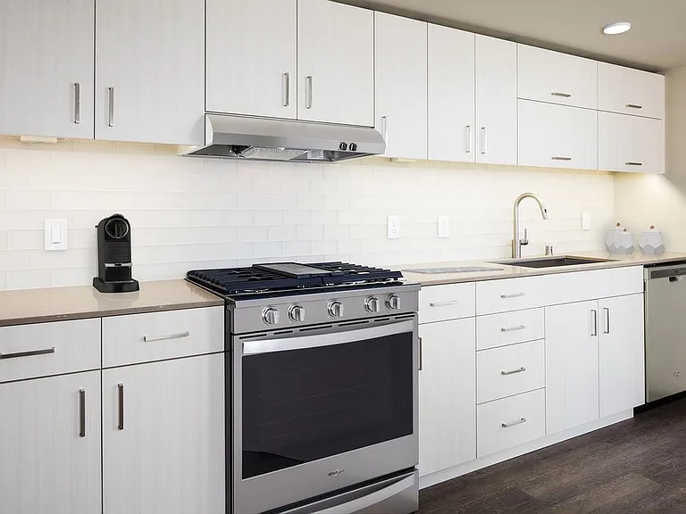 Scheme I kitchen with white cabinetry and undercabinet lighting, quartz countertops, white tile backsplash, stainless steel appliances, and hard surface flooring.