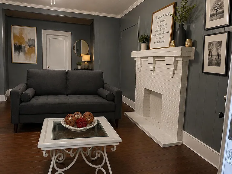 Inviting living room with dark wood floors, a comfortable sofa, ceiling fan, and a painted brick fireplace with mantel.