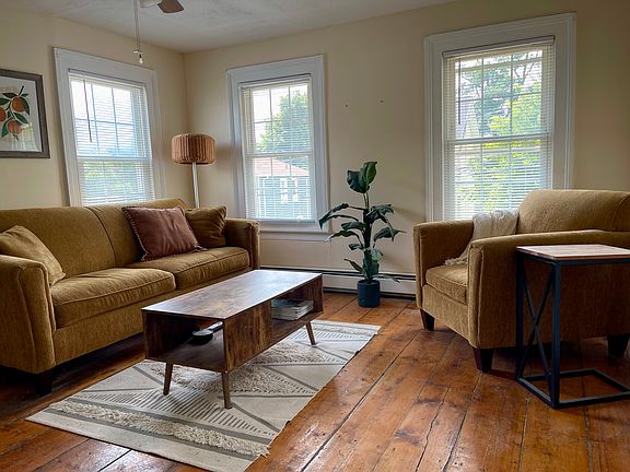 Living room with wide plank wood floors, plenty of natural sunlight, baseboard heating