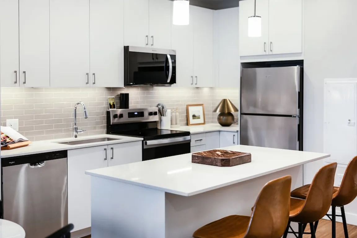 Design Collection I kitchen with stainless steel appliances, white cabinetry, grey tile backsplash, under-cabinet lighting, white quartz countertops, and hard surface flooring