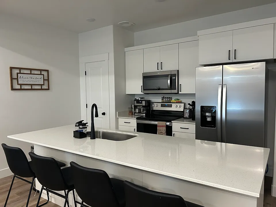Kitchen includes stove, refrigerator and bar stools.