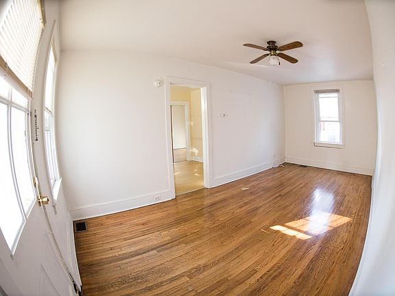 Spacious Living Room updated with new fan. You're looking into the kitchen. Kitchen now has gray paint and kitchen floors are being redone.
