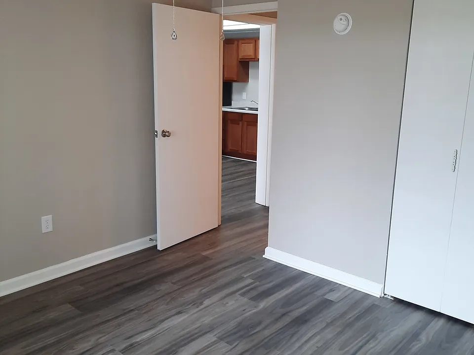 Bedroom in one bedroom apartment with a double door leading to the closet and gray VCT flooring. A ceiling fan with a light is also pictured