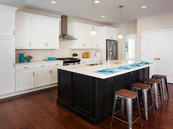 Kitchen with white cabinetry, large center island with dark base cabinets and stools at bar overhang